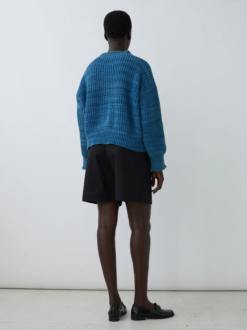Model wearing blue textured sweater and relaxed-fit black Bermuda shorts from Shaina Mote, showcasing a stylish back view.