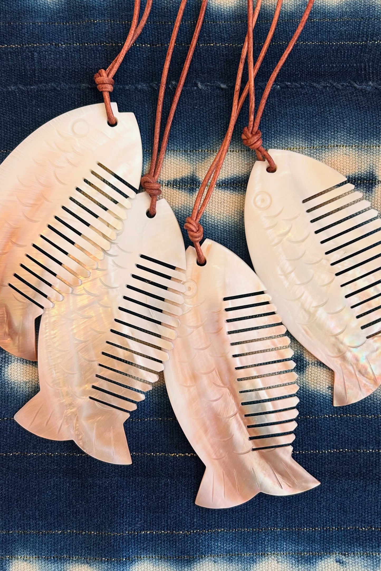 Three fish-shaped combs with leather straps on a blue fabric background