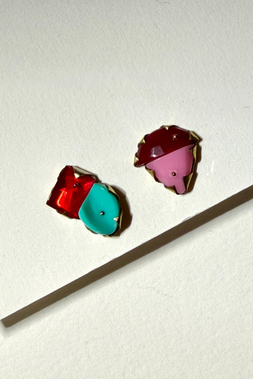 Two small enamel pin charms on a textured off-white background, one shaped like a red and turquoise ice cream cone and the other like a pink and dark red ice cream cone with gold metal trim.