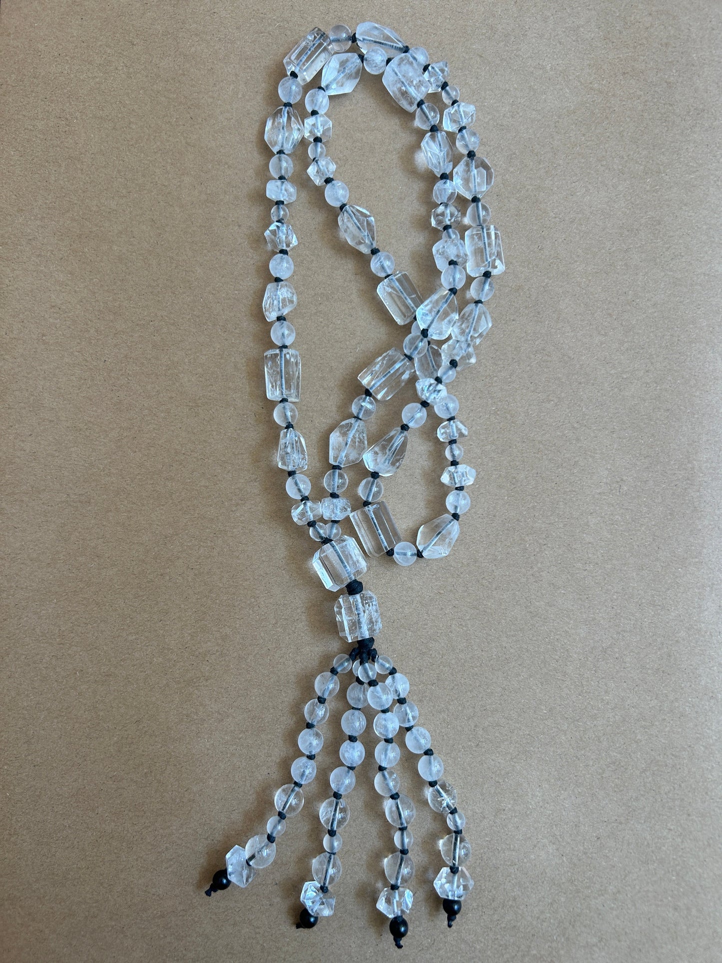 A beaded necklace made of clear faceted glass beads strung on black cords, laid flat on a brown kraft paper background.