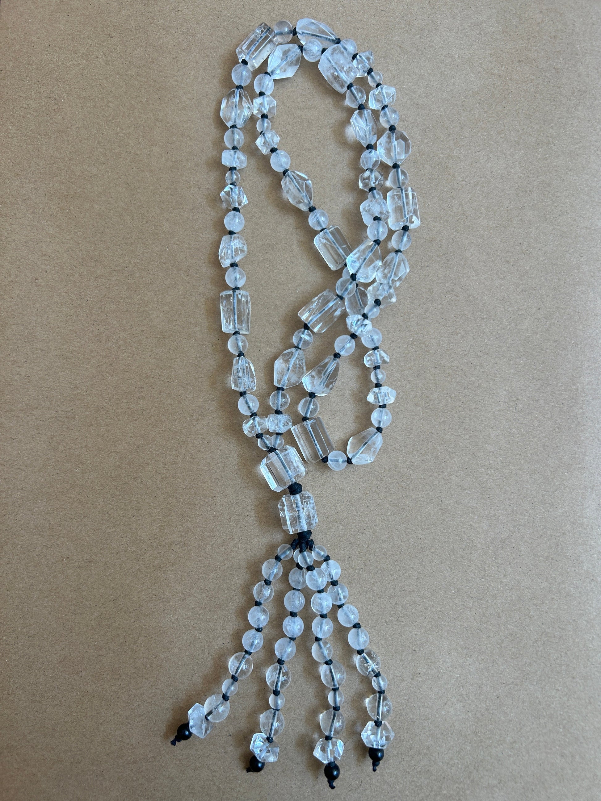 A beaded necklace made of clear faceted glass beads strung on black cords, laid flat on a brown kraft paper background.