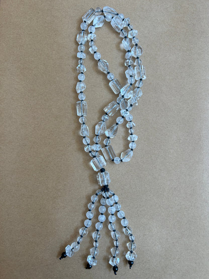 A beaded necklace made of clear faceted glass beads strung on black cords, laid flat on a brown kraft paper background.