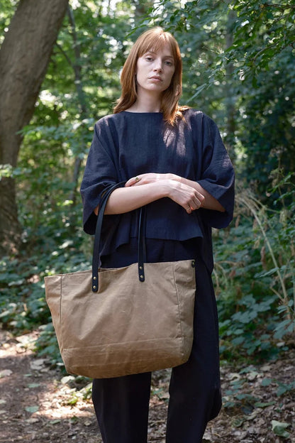 Woman holding a beige tote bag in a forest setting