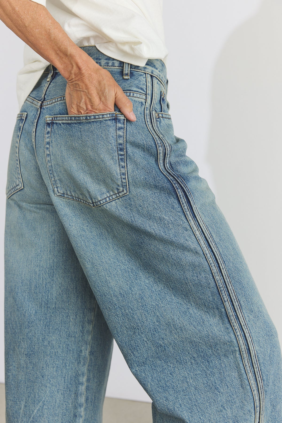 Close-up of a person wearing light blue wide-leg denim jeans with a white shirt, showing the back pocket and side seam details.