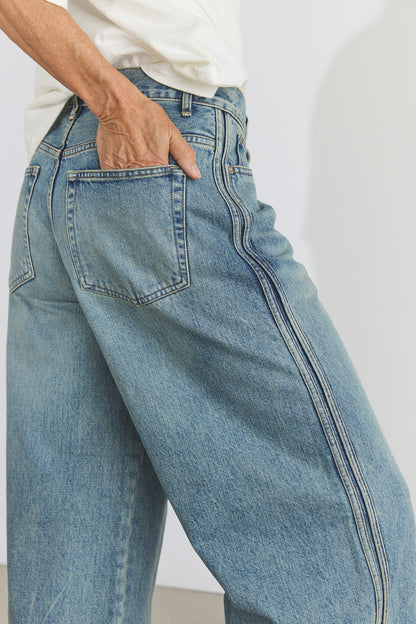 Close-up of a person wearing light blue wide-leg denim jeans with a white shirt, showing the back pocket and side seam details.