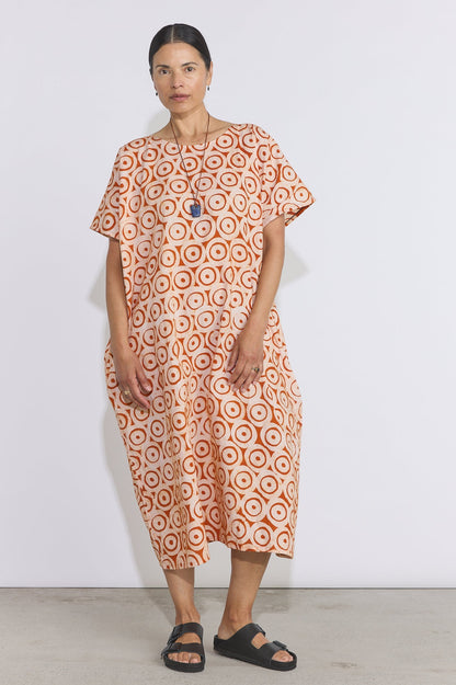 Woman wearing an orange and white patterned dress against a white background